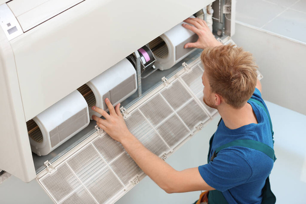 Professional technician maintaining modern air conditioner indoors - Foto, Imagen