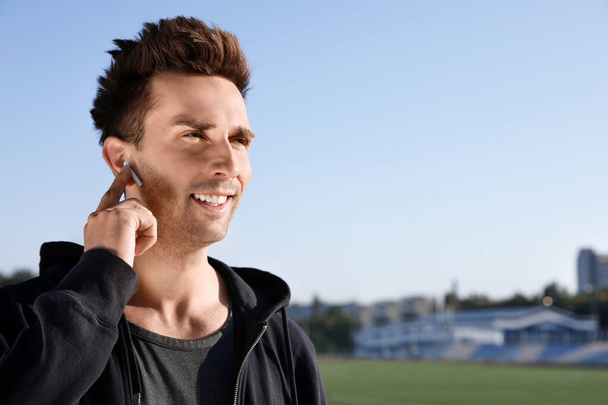 Young sportsman with wireless earphones at stadium - Fotoğraf, Görsel