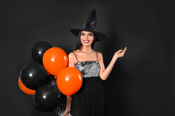 Beautiful woman wearing witch costume with balloons for Halloween party on black background - Fotografie, Obrázek