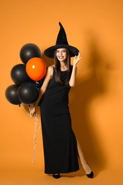 Beautiful woman wearing witch costume with balloons for Halloween party on yellow background - Photo, Image