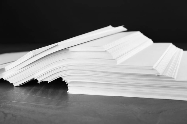 Stack of blank paper on grey stone table against black background - 写真・画像