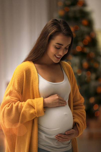 Happy pregnant woman and Christmas tree on background. Expecting baby - Foto, Bild