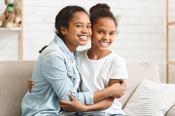 Dos encantadoras hermanas afroamericanas abrazándose en casa
 - Foto, Imagen