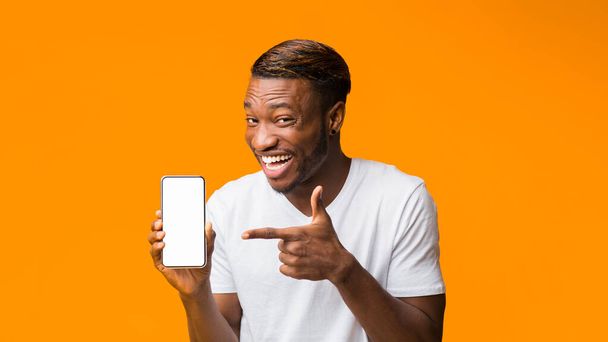 Zwarte man toont telefoon Blanco scherm staand, Oranje achtergrond, Mockup - Foto, afbeelding