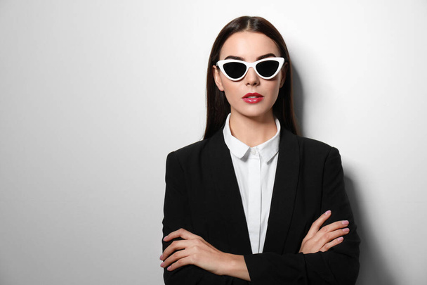 Young businesswoman in stylish sunglasses on light background, space for text - 写真・画像