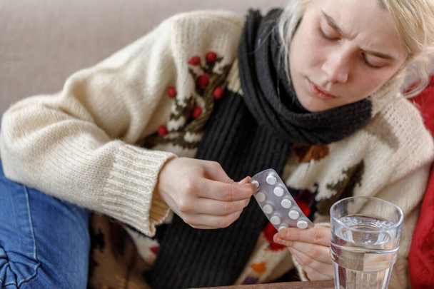 The girl in the sweater is sick lying on the couch. Colds and flu. The patient caught a cold, feeling sick and uses pills for treatment. Unhealthy girl. - Photo, Image