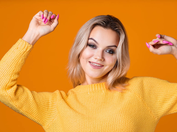 Happy and cheerful blonde in a yellow sweater on a yellow background. Positive young woman rejoices and dances, - Foto, imagen