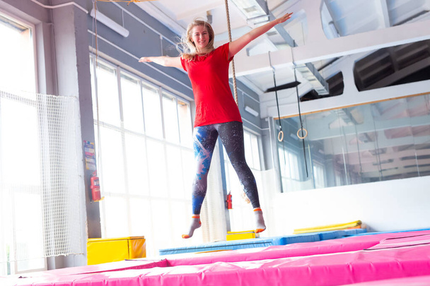 Fitness, fun, leisure and sport activity concept - Young happy woman jumping on a trampoline indoors - Fotografie, Obrázek