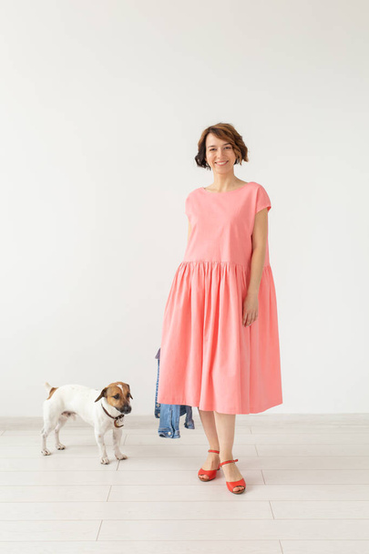 Pretty young woman in a long elegant dress and in a jeans shirt posing on a white background with her beloved dog Jack Russell Terrier. The concept of everyday stylish image. - Foto, imagen