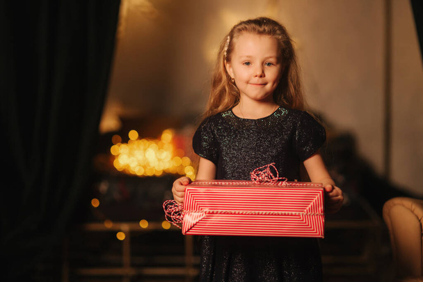 Urocza dziewczynka trzyma w rękach prezent. Boże Narodzenie w domu - Zdjęcie, obraz