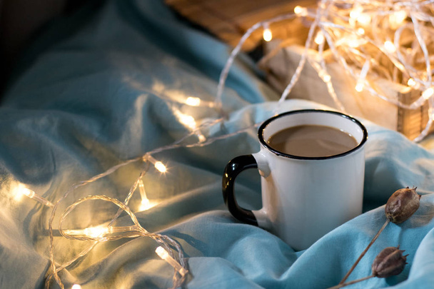Coffee cup and garland on a bed. Atmospheric hygge style. Cozy w - Fotografie, Obrázek