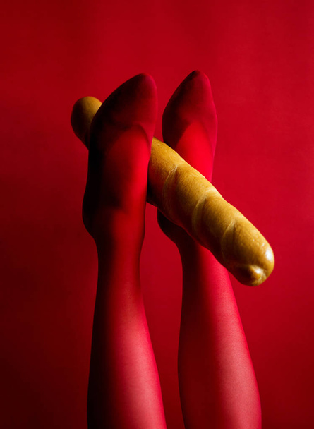 Kırmızı taytlı güzel kadın bacakları Ayaklarını kaldırmış bir baget tutuyor - Fotoğraf, Görsel