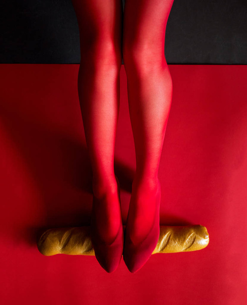 female legs in red tights hold a baguette horizontally on a red background photo - Photo, Image