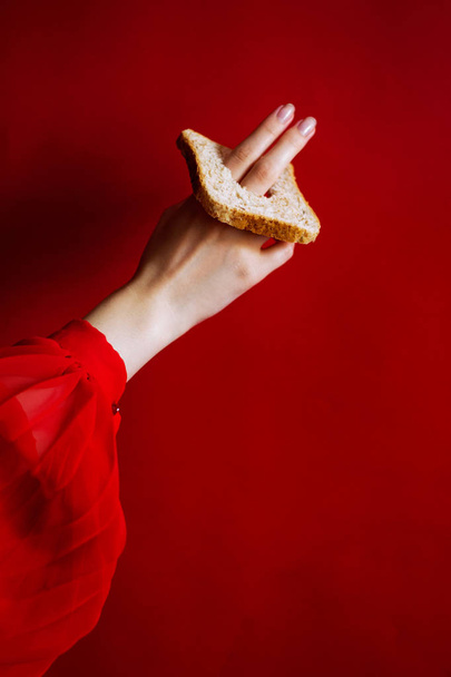 φωτογραφία θηλυκό χέρι με ένα κομμάτι λευκό ψωμί σε κόκκινο φόντο - Φωτογραφία, εικόνα
