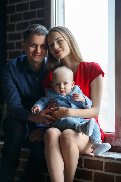 Parents and their child sitting at the window. Mom, dad and baby. Portrait of young family. Happy family life. Man was born. - Foto, Bild