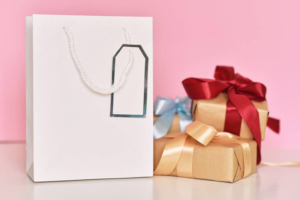 Подарочная коробка с лентой и бумажным пакетом для покупок на розовом фоне
 - Фото, изображение