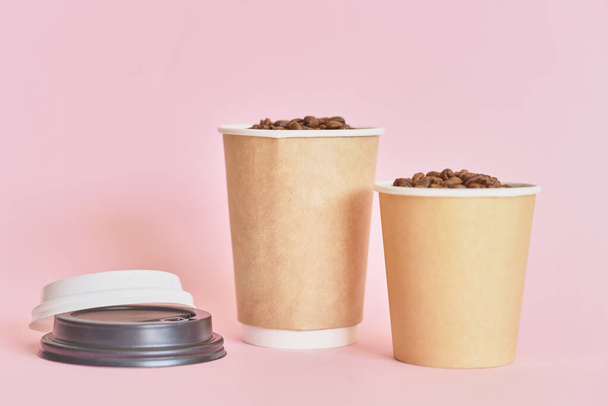 Дві паперові чашки кави з кавовими зернами на рожевому фоні
 - Фото, зображення
