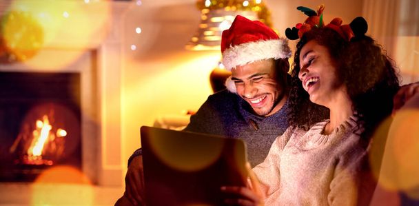 Composite image of brown parquet against couple at home using laptop at christmas time - 写真・画像