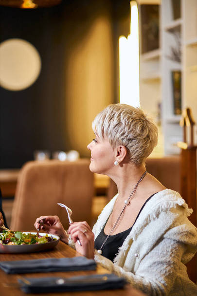 Senior woman have dinner in elegant restaurant, attentively looking at someone - Photo, Image
