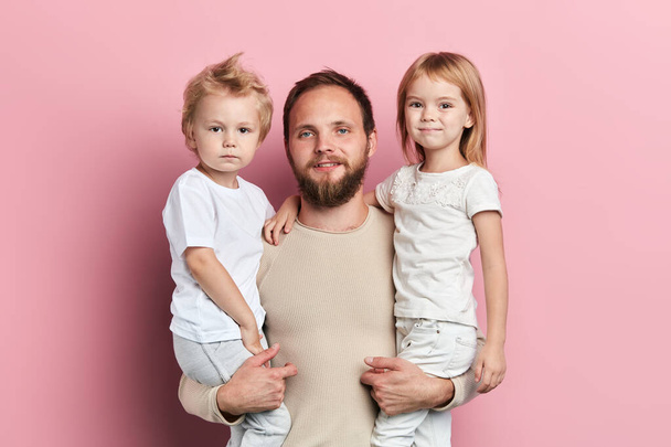 padre guapo llevando a su pequeña hija y su hijo sobre fondo rosa
 - Foto, imagen
