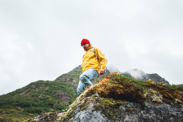Sarı ceketli ve sırt çantalı cesur bir turist açık havada dağ yürüyüşü yapıyor. Aktif gezgin yaşam tarzı seyahat tutkusu - Fotoğraf, Görsel