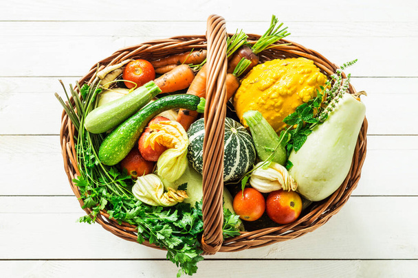 Colorful organic vegetables in wicker basket on white wood - Фото, изображение
