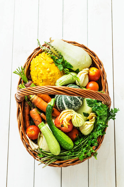 Colorful organic vegetables in wicker basket on white wood - Photo, image