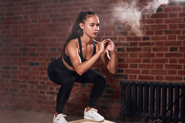 Beautiful female bodybuilder performing squats jumping on fit box in gym - Фото, зображення