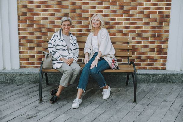 Joyous women sitting on the bench outdoors - Fotó, kép