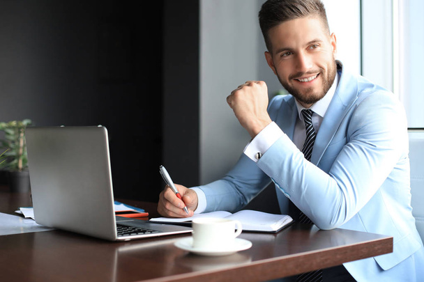 Portrait of happy businessman sitting at office desk, looking at camera, smiling - Photo, image