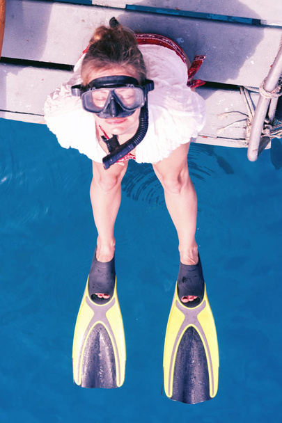 Girl in flippers, mask and with a tube sitting on the edge of th - Foto, Imagen