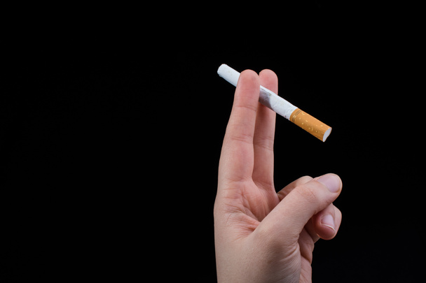 La mano sostiene un cigarrillo sobre fondo negro - Foto, Imagen