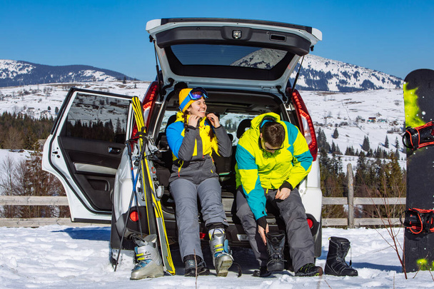 мужчина и женщина одеваются в лыжное снаряжение возле внедорожника - Фото, изображение