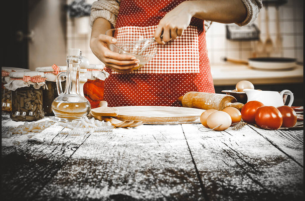 Chef's female hands preparing food on wooden table in the kitchen. Baking a cake. A woman in red apron with the kitchen background. - Фото, изображение