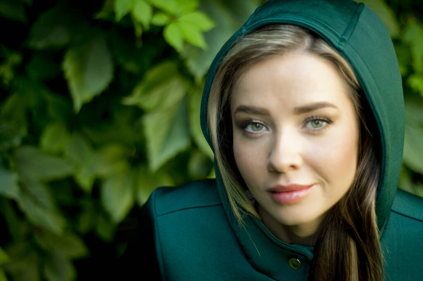 Portrait of a beautiful girl in a green coat on a background of ivy . - Zdjęcie, obraz