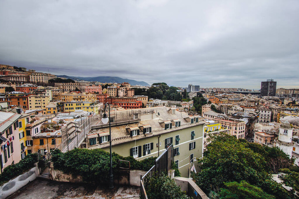 Many beautiful old italian houses painted in bright colors with mountains on the background.An amazing cityscape of some public housing in Genova built in the 60s over hills of the city in cloudy day, - Fotografie, Obrázek
