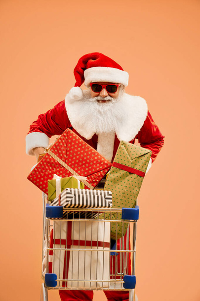 Smiling Santa Claus pushing shopping cart with gift boxes - Фото, зображення