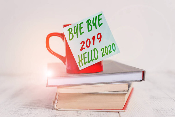 Conceptual hand writing showing Bye Bye 2019 Hello 2020. Business photo text saying goodbye to last year and welcoming another good one Coffee cup sticky note stacked books retro old retro wooden tabl - Photo, Image