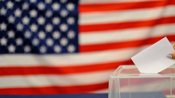 femme qui met un bulletin de vote dans une urne le jour du scrutin. Gros plan de la main avec papier de votes blancs sur fond de drapeau des Etats-Unis
. - Photo, image
