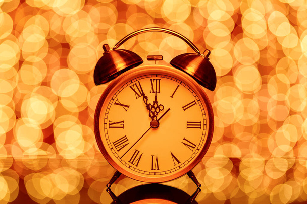 New years eve midnight. Retro alarm clock whose pointer shows five to twelve on festive bokeh background - Photo, Image