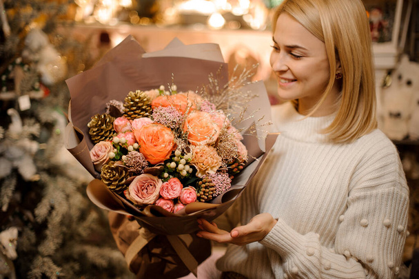 Young smiling girl holding a bouquet of pink and orange roses decorated with golden cones - 写真・画像