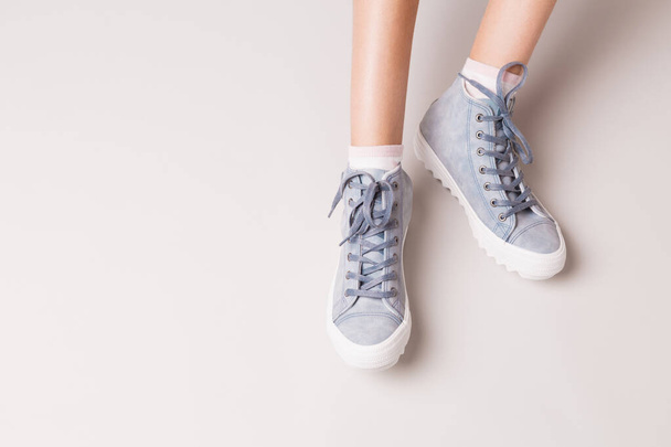 Pastel blue sneakers on legs. Casual footwear on grey. - Fotoğraf, Görsel
