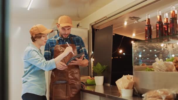 Los empleados exitosos de Food Truck Man and Woman en gorras marrones están usando una computadora de tableta. Discuten sus ganancias y planes de negocio futuros. Camión comercial o quiosco que vende comida y bebidas callejeras
. - Imágenes, Vídeo