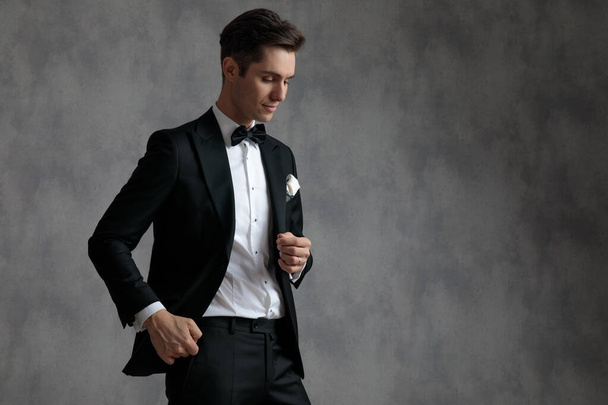 young elegant man in tuxedo holding hands in pocket and looking  - Fotografie, Obrázek
