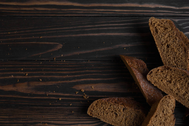 Zwart brood. Een gesneden donkere stokbrood ligt op een houten ondergrond van donkerbruine planken. - Foto, afbeelding