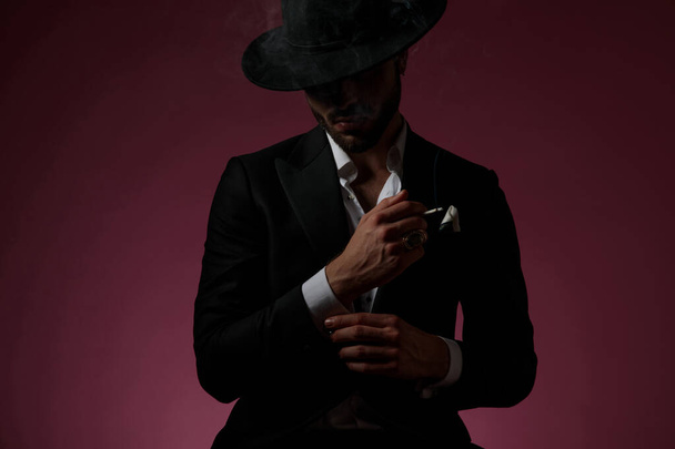 Rejtélyes férfi rögzíti az ingujját és elszív egy cigarettát. - Fotó, kép