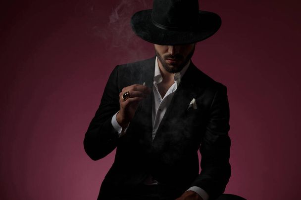 Komoly kinézetű titokzatos férfi cigarettázik. - Fotó, kép