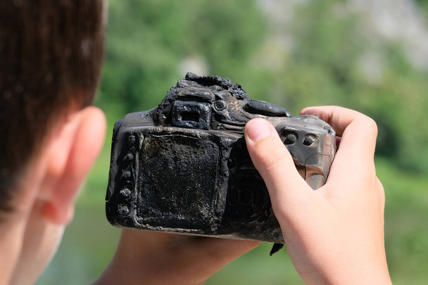 Hő vagy a tűz hatása. A kamera elolvadt egy tinédzser kezében. Közelkép. Furcsa helyzet a természetben. Fényképezés egy égett eszközzel. - Fotó, kép