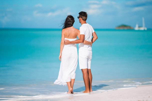 Jovem casal caminhando na praia tropical com areia branca e água azul-turquesa do oceano na ilha de Antígua, no Caribe
 - Foto, Imagem