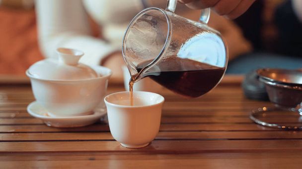 中国茶の儀式、少女のティーポットから木製のテーブルの上にカップに紅茶プーアル茶を注ぐ、閉じる - 写真・画像